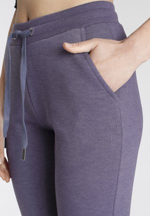 Purple sweatpants featuring a ribbed waistband, drawstring closure with metal tips, and side pockets for functionality. Soft textured fabric.