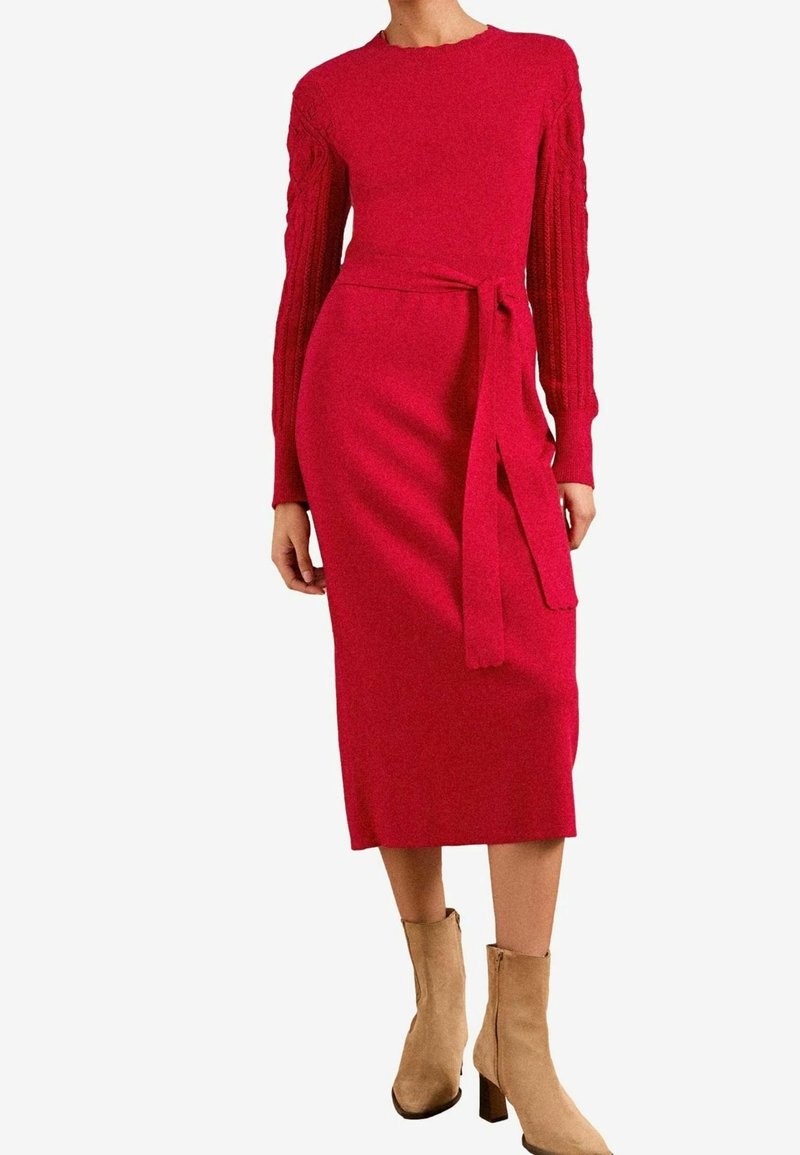 Robe midi rouge à manches longues avec texture tricotée, ceinture à la taille et bottines en daim beige sur une personne debout.