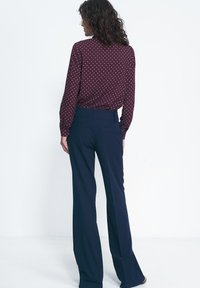 Buraczkowa bluzka w kropki z długimi rękawami, w zestawie z granatowymi spodniami o szerokich nogawkach. Bluzka ma luźny krój i subtelną teksturę.