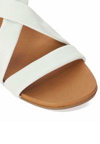White leather slide sandal with crisscross straps and a light brown, textured sole. The straps feature a soft, pebbled finish.