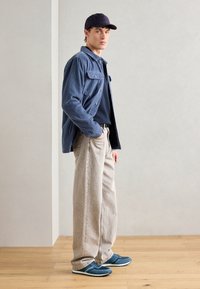 Camisa de cotim azul, t-shirt azul-marinho, calças largas bege e ténis azuis. O conjunto apresenta um estilo casual com cores e texturas contrastantes.