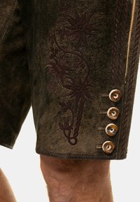 Pantalones cortos de cuero marrón con intrincados bordados florales en marrón oscuro a lo largo del lateral y cinco botones decorativos, con detalle de superficie texturizada.