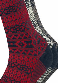 Drei Paare gestrickte Socken: ein rotes Paar mit schwarzen geometrischen Mustern, ein cremfarbenes Paar mit dunklen Mustern und ein dunkelbraunes Paar mit hellen Mustern.