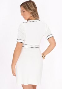 Weißes Strickkleid mit kurzen, strukturierten Ärmeln und schwarzem Saum. Figurbetonter Oberteil mit leicht ausgestellt Rock. Schlichtes, modernes Design.