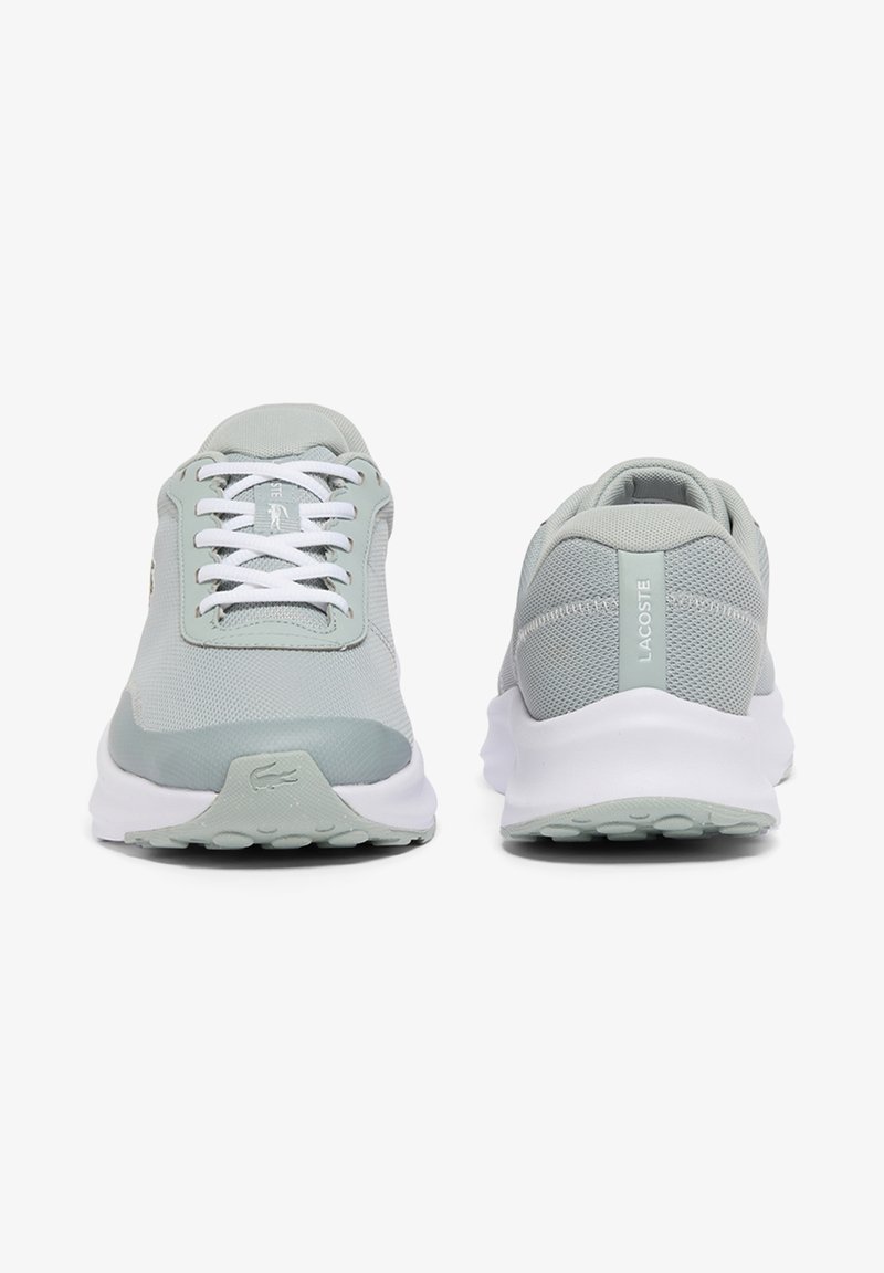 Paire de baskets de sport gris clair avec semelles blanches, vues de face et de dos, avec le logo Lacoste sur la languette et la bride du talon.