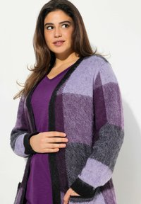 Lila kariert Strickjacke aus weichem, strukturiertem Stoff mit schwarzen Akzenten, offener Front, langen Ärmeln und seitlichen Taschen.
