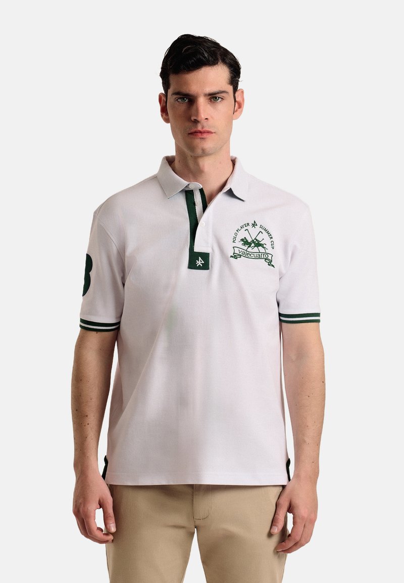 Camisa polo blanca con detalles verdes. Presenta una tapeta de tres botones, un logo bordado en el pecho y puños a rayas. Mangas cortas.