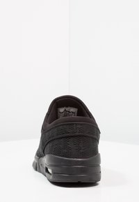 Chaussure de sport noire avec une tige en mesh, une semelle flexible et un col rembourré. Présente un talon arrondi et un marquage minimaliste sur la doublure intérieure.