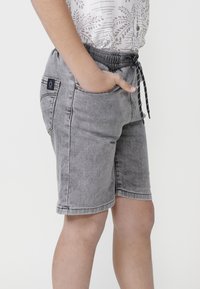 Pantalones cortos de mezclilla gris con cintura elástica, cordones ajustables y diseño de costura de contraste; cuenta con bolsillos laterales y una etiqueta con el logo.