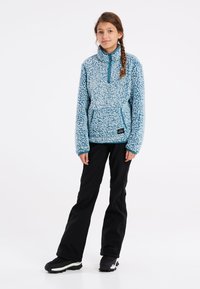 Ljusblå fleecepullover med texturerad yta, halvdragkedja och känguruficka. Kombineras med svarta byxor och svarta skor.