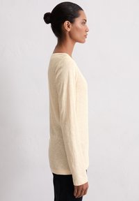 Chemise longue à manches jaunes claires avec une coupe décontractée et un col rond, dotée d'un tissu doux et texturé et d'un motif chiné subtil.