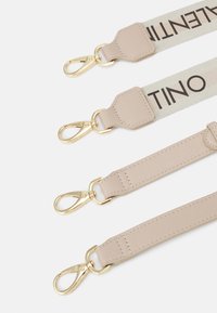 Curele din țesătură bej cu clipsuri metalice aurii, având un logo proeminent "VALENTINO". Textură netedă, design curat și accesorii durabile.