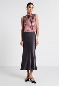 Top senza maniche a righe rosse e bianche con un nodo al collo, abbinato a una lunga gonna nera in raso lucido. Texture liscia e design moderno.