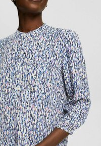 Blouse à manches longues avec un motif mixte bleu, rose et blanc. Encolure ronde avec des boutons à l'avant. Tissu doux et texturé.