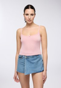 Top tinta rosa chiaro a coste con spalline sottili e dettaglio a fiocco frontale, abbinato a una mini gonna di denim blu sbiadito con orli sfrangiati.