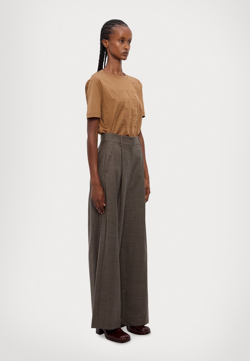 Camiseta de algodón marrón con texto en relieve, combinada con pantalones de cuadros grises de pierna ancha y zapatos de plataforma burdeos.