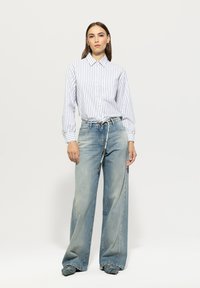 Striped button-up shirt in white and navy, paired with light blue wide-leg jeans. Features a belt with a woven detail and minimal pockets.