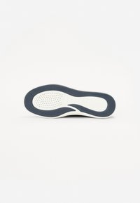 Sole di sneakers in bianco e nero, caratterizzata da un design testurizzato con scanalature e fori di ventilazione. Forma curva con un bordo spesso.