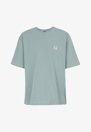 Hellblaues oversized T-Shirt mit kurzen Ärmeln, Rundhalsausschnitt und kleinem weißem quadratischem Aufnäher mit gekreuzten Werkzeugen auf der linken Brust.