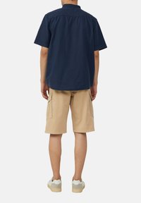 Korte mouw marineblauwe shirt met een kraag aan de achterkant, gecombineerd met beige cargo shorts met zijzakken en lichte sneakers.