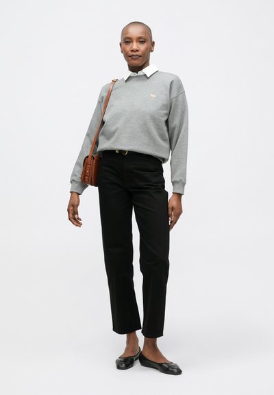 Sudadera gris con cuello blanco y un pequeño logo naranja, combinada con pantalones negros de pierna recta y zapatos planos negros. Bolso cruzado marrón.