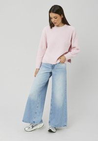 Pull en tricot rose clair à coupe décontractée, associé à un jean bleu délavé à jambes larges. Chaussures : baskets argentées réfléchissantes.