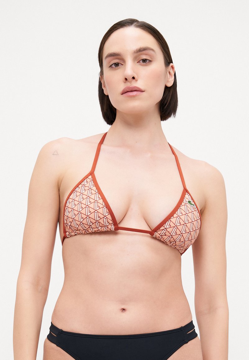 Triangular bikini top with geometric pattern in red and beige, featuring thin straps. Includes a small logo detail on the left side.