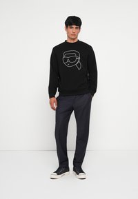 Felpa nera con una grafica bianca di un volto che indossa occhiali da sole, abbinata a pantaloni scuri e sneakers nere con suola bianca.