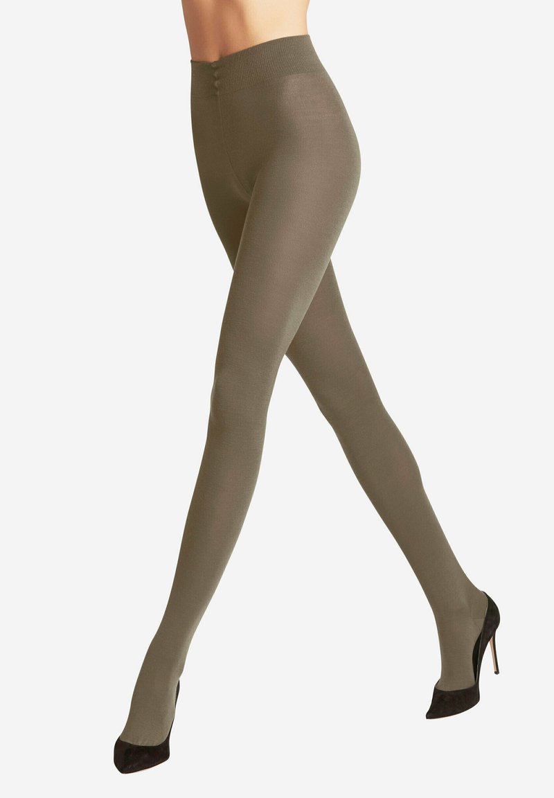Leggings vert olive avec une large ceinture, texture lisse et forme ajustée, associés à des chaussures à talons noirs.