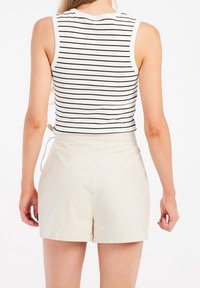 Vit linne med svarta ränder, parat med ljusbeige shorts. Shortsen har en mjuk textur och en avslappnad passform.