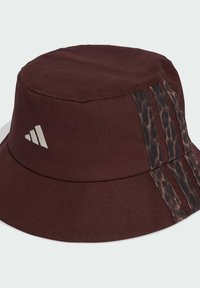 Brauner Bucket Hat aus Stoff mit glatter Textur, versehen mit zwei Leopardenmusterstreifen und einem weißen Logo auf der Vorderseite.