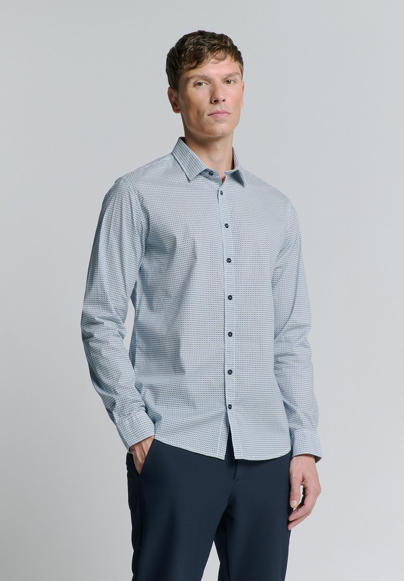 Chemise à boutons bleue à motifs avec un col, manches longues et boutons foncés, associée à un pantalon sombre. Texture lisse.
