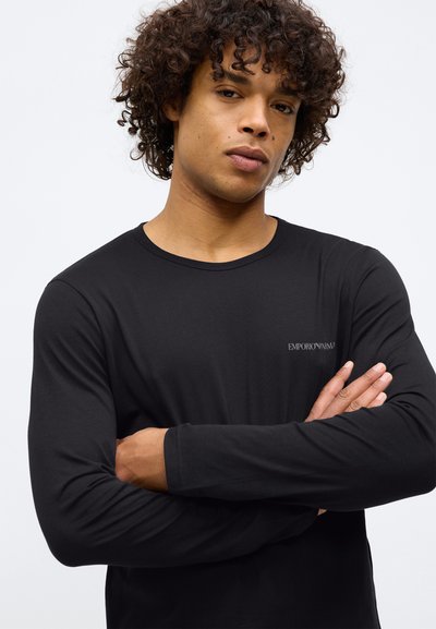 Camisa preta de mangas compridas feita de um tecido leve e suave. Apresenta um decote redondo e um pequeno logotipo branco na área do peito esquerdo.