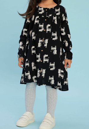 Schwarzes Kleid mit weißem Zebra-Print, langen Ärmeln, Knopfverschluss und gerafftem Detail. Kombiniert mit hellgrauen strukturierten Strumpfhosen und weißen Schuhen.
