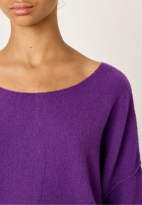 Lilla striktrøje med bred udskæring, drop shoulder-design og blød tekstur. Materialet virker fluffy og let.