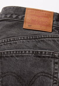 Poche arrière d'un jean Levi's 501 noir avec coutures surpiquées et étiquette en cuir beige Levi Strauss & Co. au-dessus de la poche.