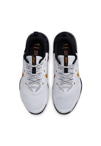 Zapatillas deportivas blancas con parte superior de malla texturizada, forro negro, acentos naranjas y una suela flexible. Presentan un sistema de cordones tradicional.