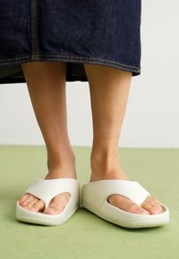 Sandali infradito in gomma bianca con un design a fasce larghe e suole texturizzate, che mostrano uno stile open-toe.
