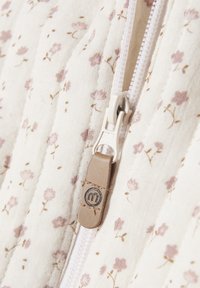 Tessuto trapuntato con piccoli motivi floreali rosa; una cerniera bianca con un tirante in pelle beige che mostra un dettaglio del logo.