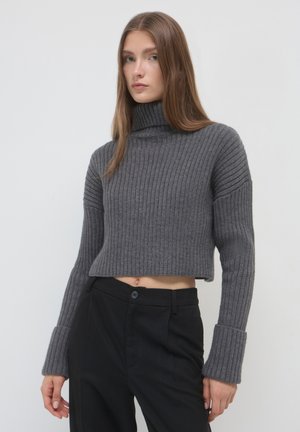 Gekürzter grauer Rippstrickpullover mit hohem Kragen, langen Ärmeln mit breiten Bündchen und weichem Material, kombiniert mit schwarzen Hosen.