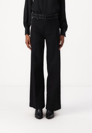 Pantaloni neri a gamba larga realizzati in tessuto resistente, con vita alta e una cintura nera con borchie. Abbinati a eleganti stivaletti neri alla caviglia.