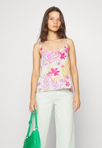 Top de flores com padrões em rosa e amarelo, feito de um tecido leve. Combinado com calças verde claro e uma bolsa texturizada verde.