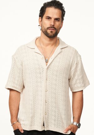 Beige short-sleeve shirt made of textured knit fabric, featuring a zigzag pattern and a collaredneckline with front buttons.