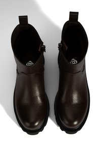Bottines en cuir marron avec une finition texturée, présentant un design courbé, des fermetures éclair latérales et une semelle en caoutchouc noire.