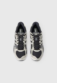 Παπούτσια τρεξίματος Asics με μαύρο διχτυωτό άνω μέρος, μπεζ λεπτομέρειες και γκρίζες λεπτομέρειες. Διαθέτουν κορδόνια και μαξιλαρωτή σόλα για υποστήριξη.