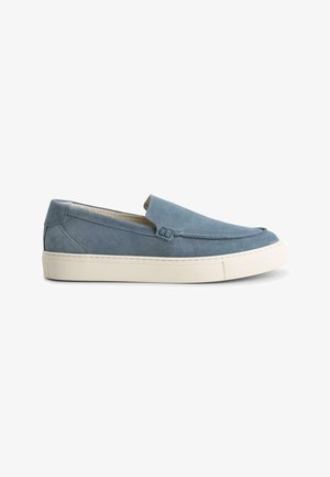 Zapatos slip-on de ante azul con una suela de goma blanca plana, que presentan costuras mínimas y un diseño simple. Sin cordones ni herrajes visibles.