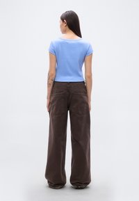 Ελαφριά γαλάζια κοντομάνικη εφαρμοστή μπλούζα συνδυασμένη με φαρδιά καφέ παντελόνια με δύο πίσω τσέπες. Ορατές υφές υφάσματος στα ρούχα.