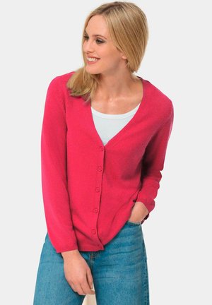 Helles pinkes Cardigan mit V-Ausschnitt, Knopfverschluss und langen Ärmeln. Getragen über einem hellblauen Oberteil, kombiniert mit blauen Jeans. Weiche Textur.