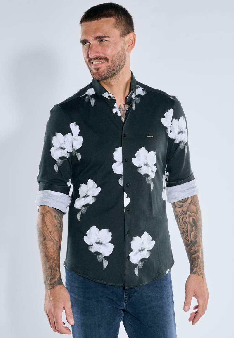 Schwarzes Hemd mit weißem Blumenmuster, mit Knopfkragen, hochgekrempelten Ärmeln, aus einem Stoff mit glatter Textur, getragen mit blauen Jeans.