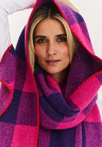 Szalik z mieszanki wełny z dużym wzorem w kratę w odcieniach różu i fioletu, z czerwonym przeszyciem na brzegu, miękką teksturą i luźnym krojem.